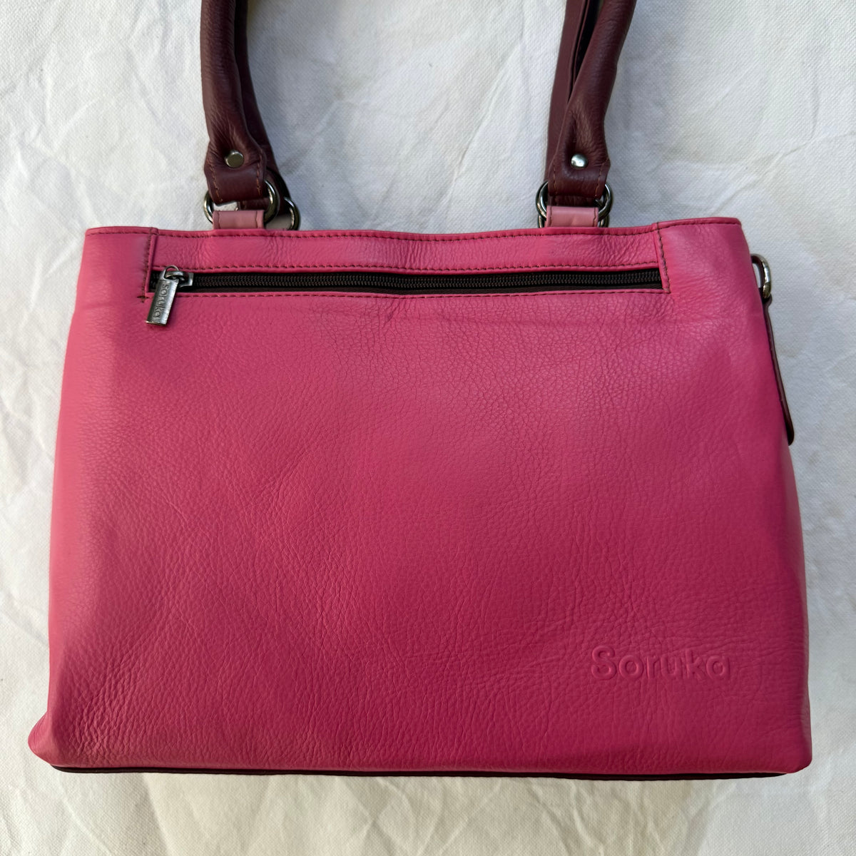 pink leather handbag with top zipper pocket and 2 maroon shoulder straps