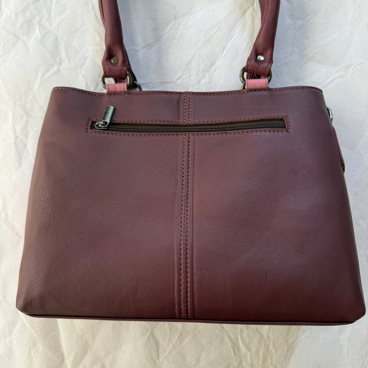 other side of handbag with burgundy leather backing and zipper pocket across the top