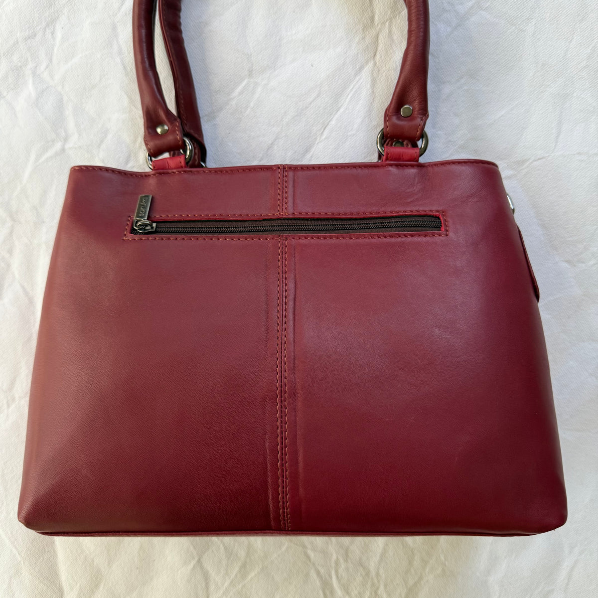 A deep red leather handbag with double shoulder straps and a front zippered pocket