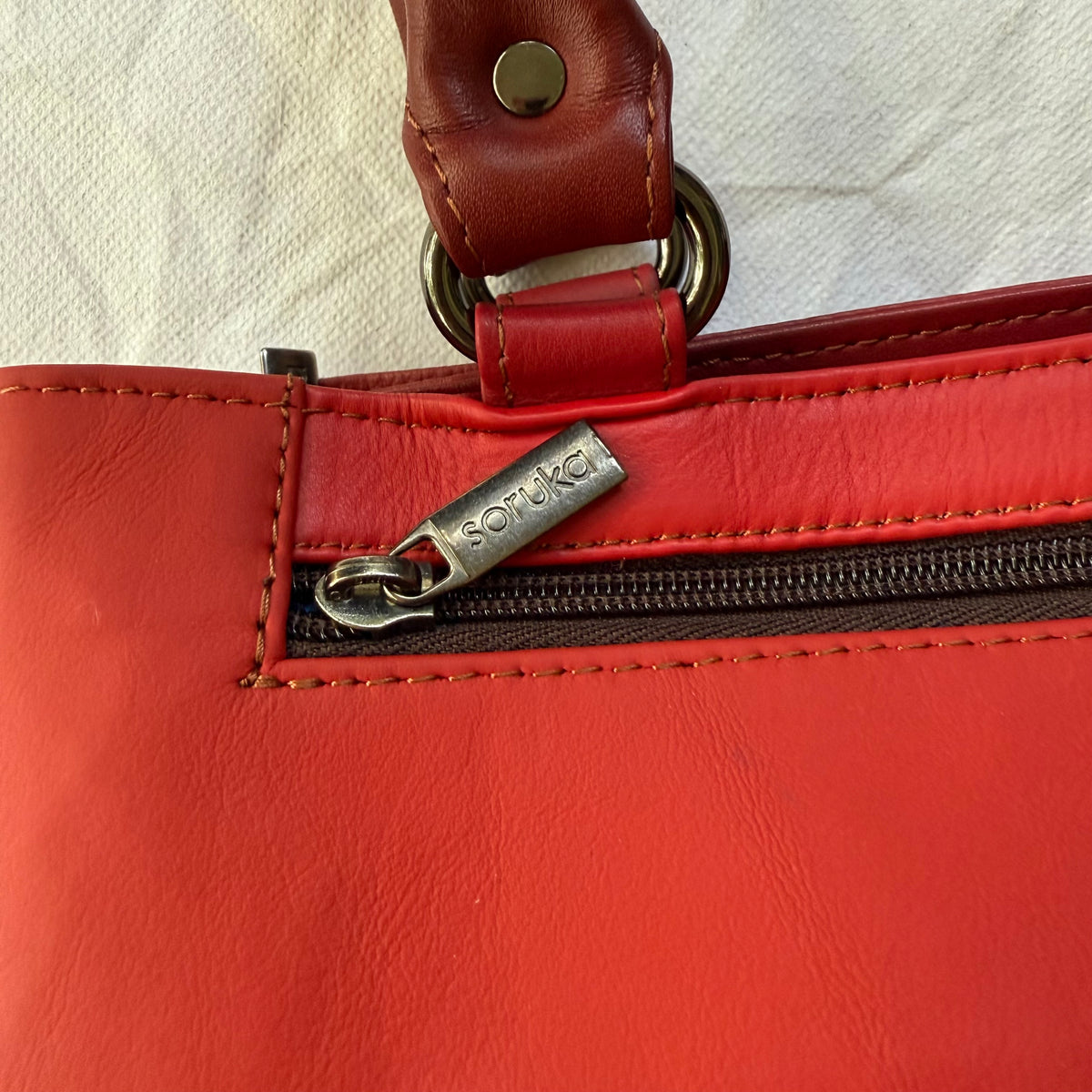 Close-up of a red leather handbag showing a zippered pocket