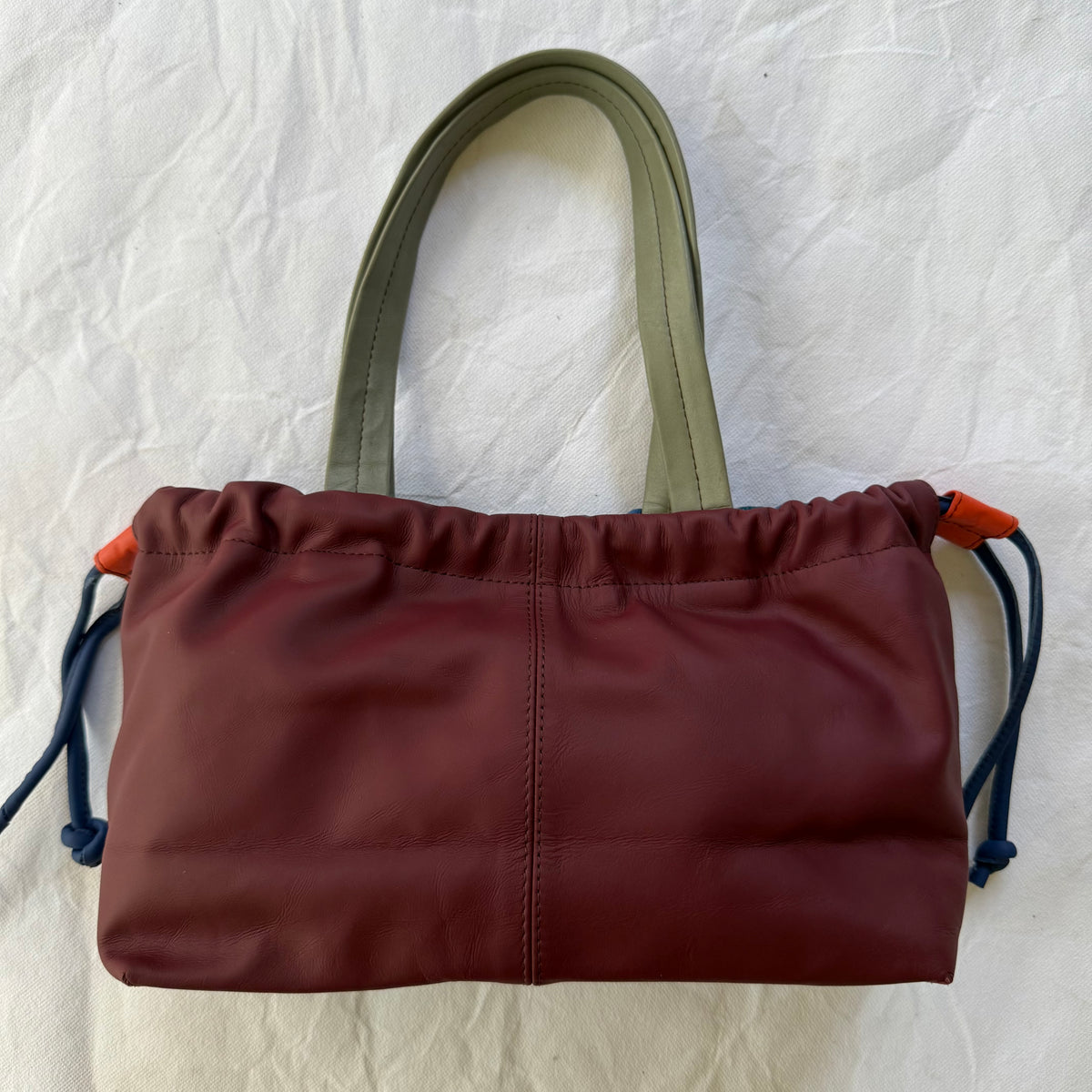 burgundy handbag with cinched design and grey handles