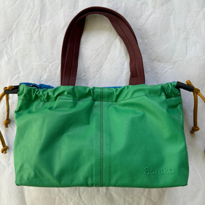 green handbag with cinched design and maroon handles