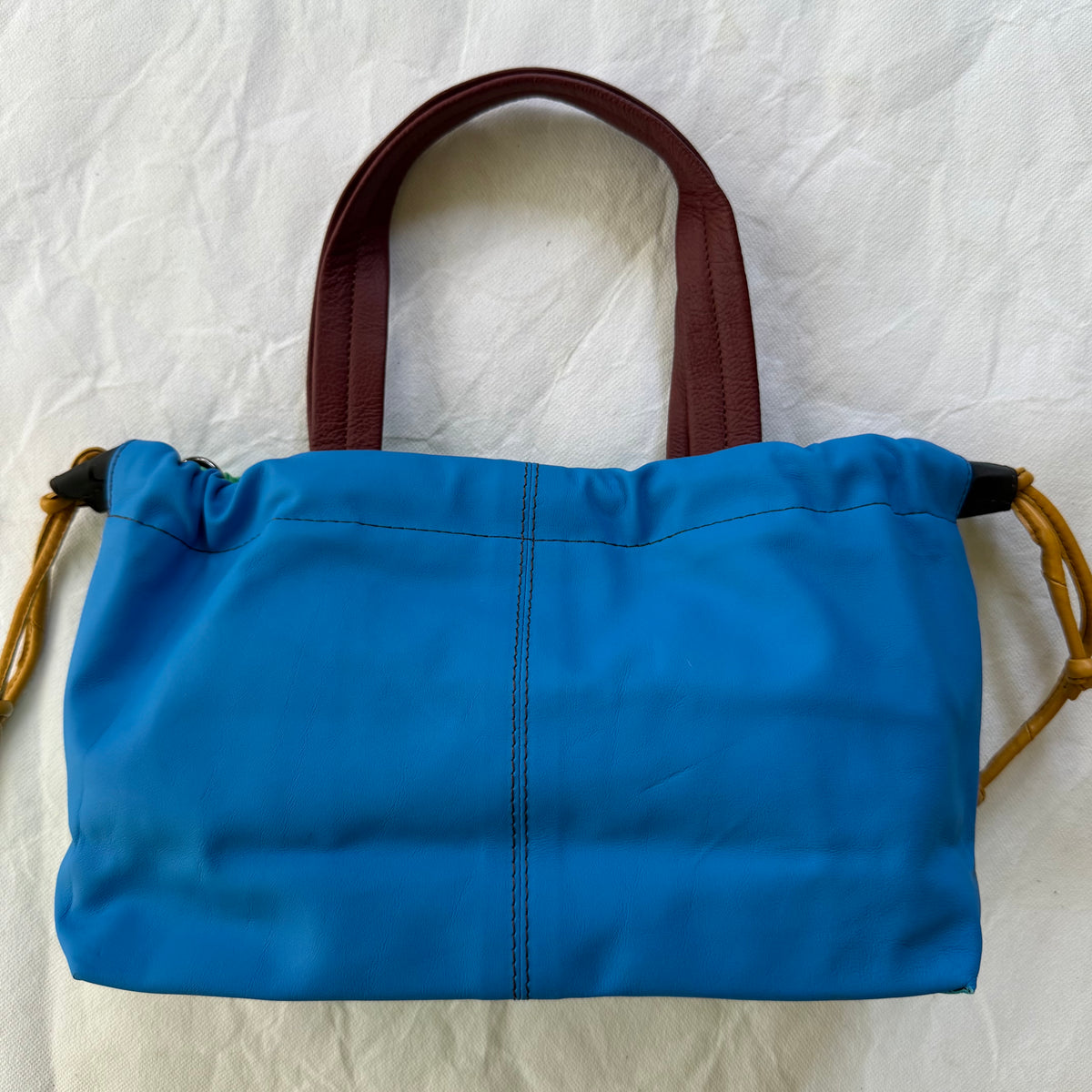 other side on handbag showing bright blue leather and maroon handles