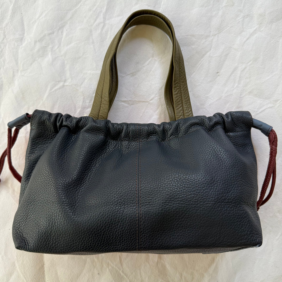 navy handbag cinched slightly across the top with taupe-green handles