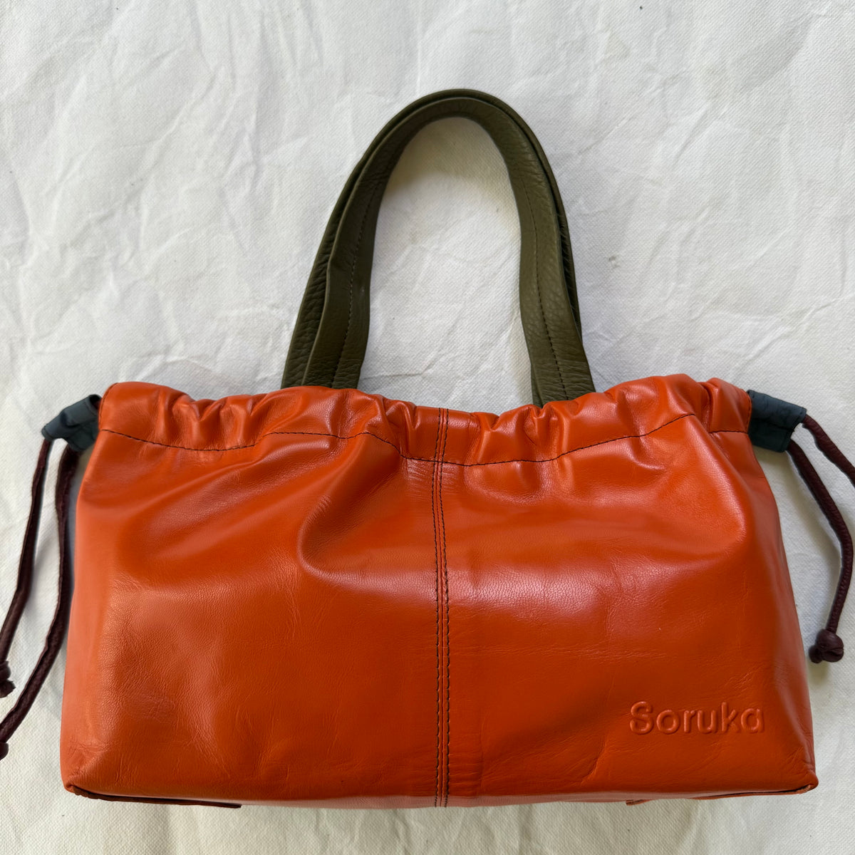 other side of handbag with vibrant orange leather and taupe-green handles.