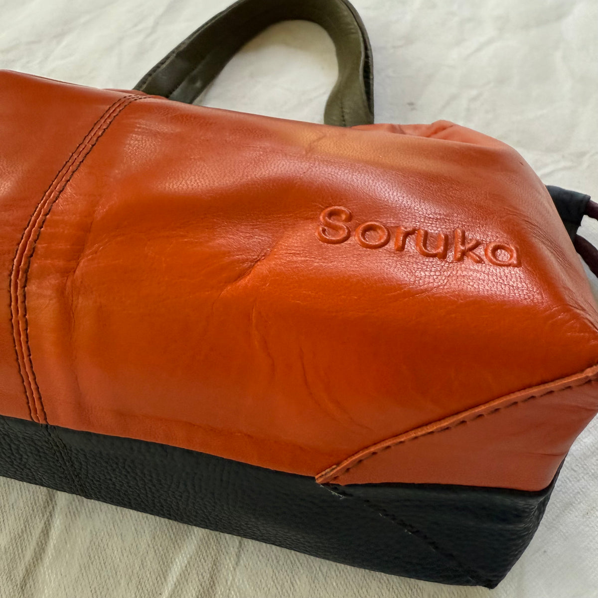 bottom view of orange and navy handbag with 'soruka' embossed in the  bottom corner of front of bag