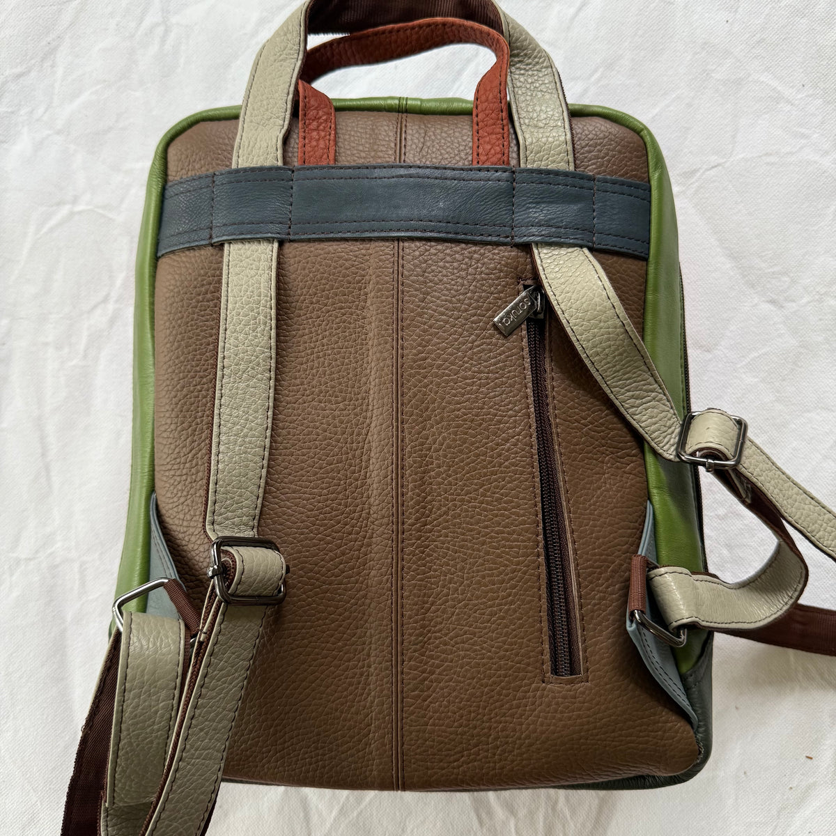 brown pebbled leather backpack shown from the back, featuring a central vertical seam, a vertical zippered pocket, dual top handles, and adjustable shoulder straps in beige and dark gray, with olive green side panels.