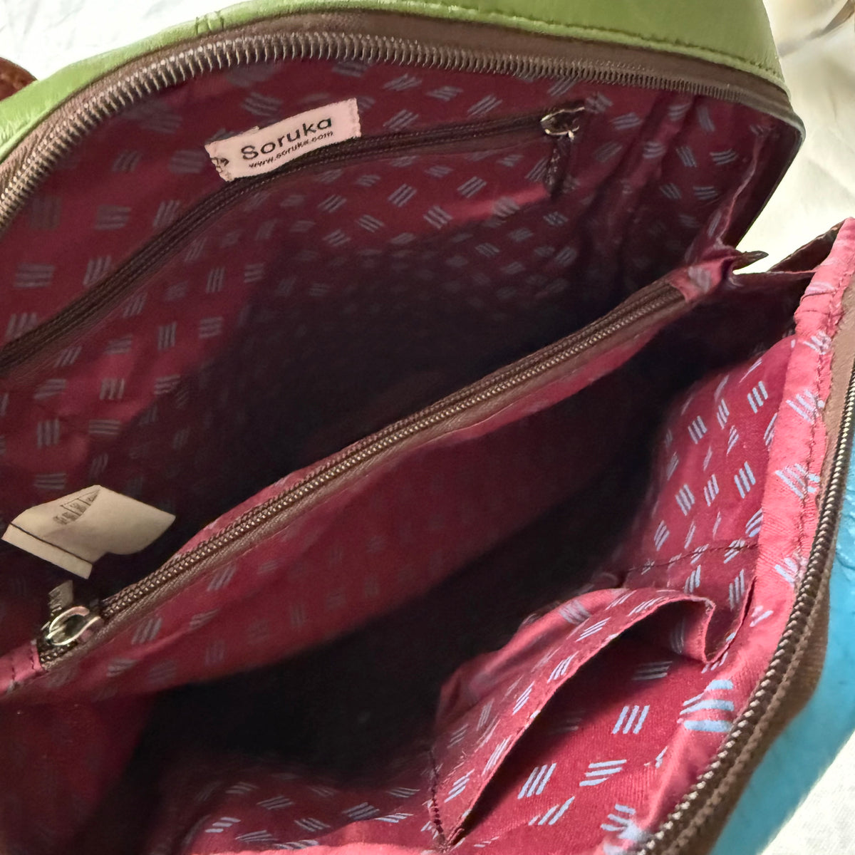 Close-up of the interior of a backpack, showing a maroon patterned lining with a zippered pockets