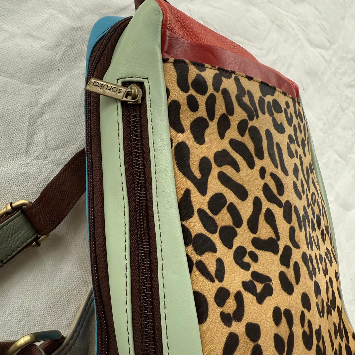 side view of backpack with mint green side panel with a brown zipper in it