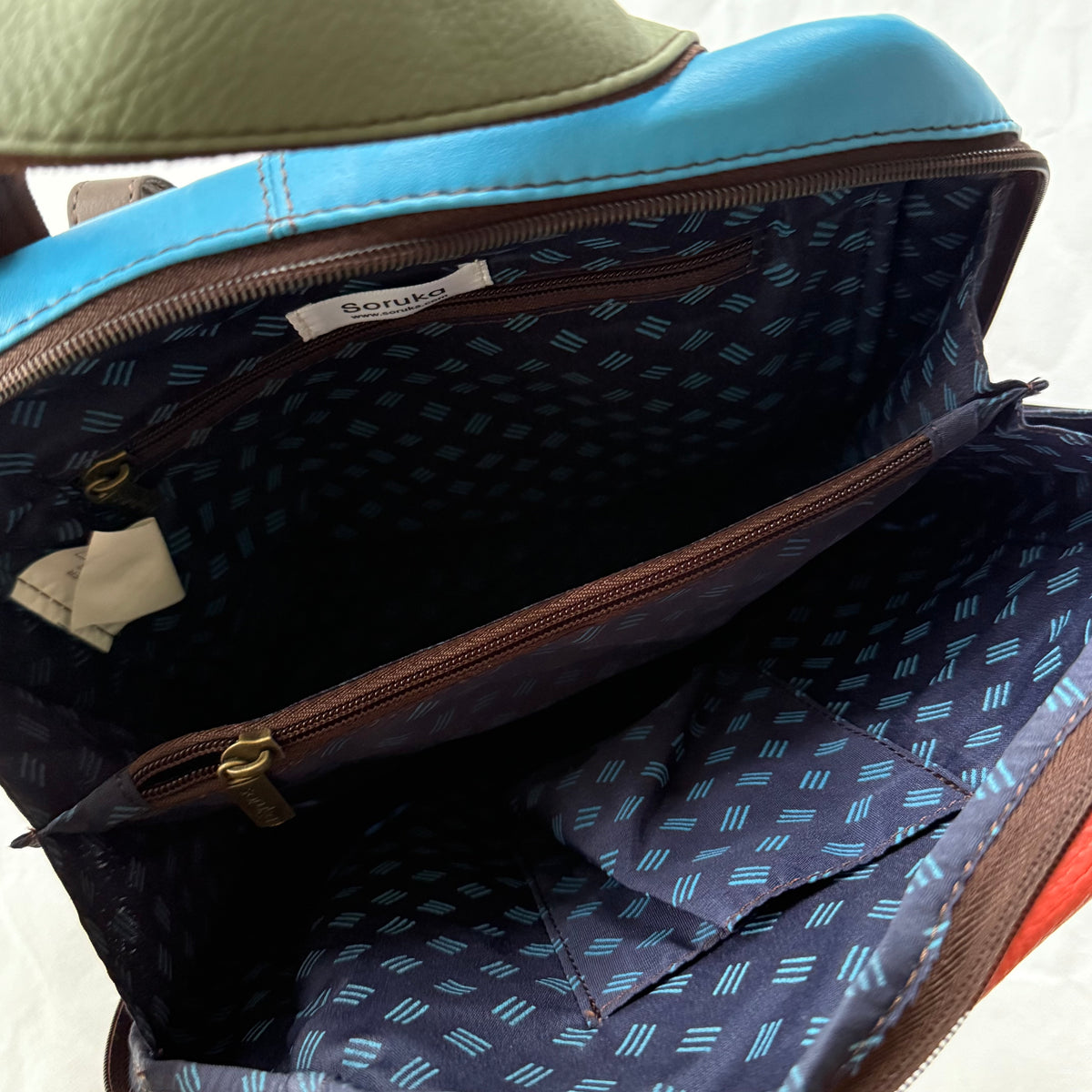 Close-up of the interior of backpack, showing a patterned navy lining with light blue accents, a zippered pocket