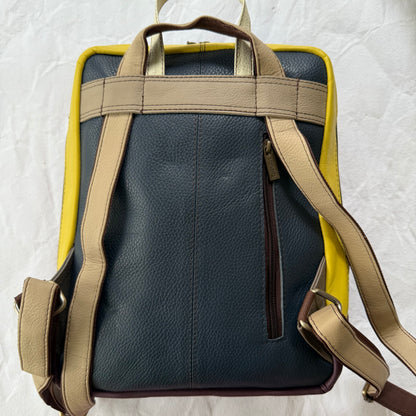 back view of backpack show dark leather section, yellow rim, vertical zippered pocket, and light bige shoulder straps