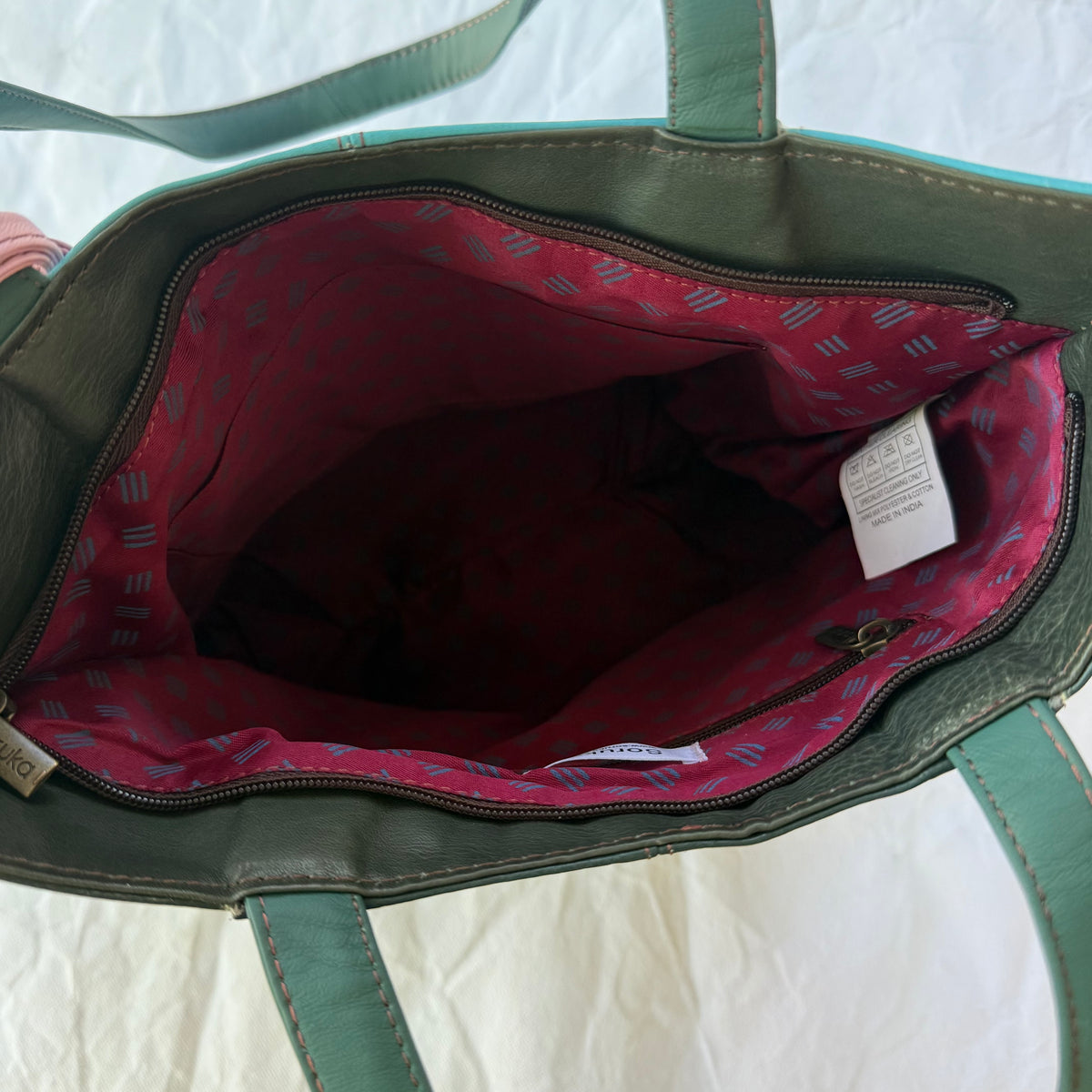 interior view of tote showing maroon patterned lining, zip and slip pockets, and top zipper closure