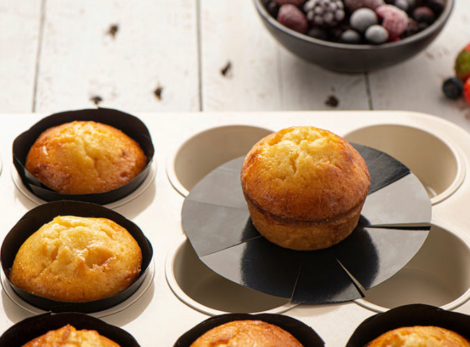 muffins in muffin pan with muffin liners and one muffin set on top of pan with liner peeled away.