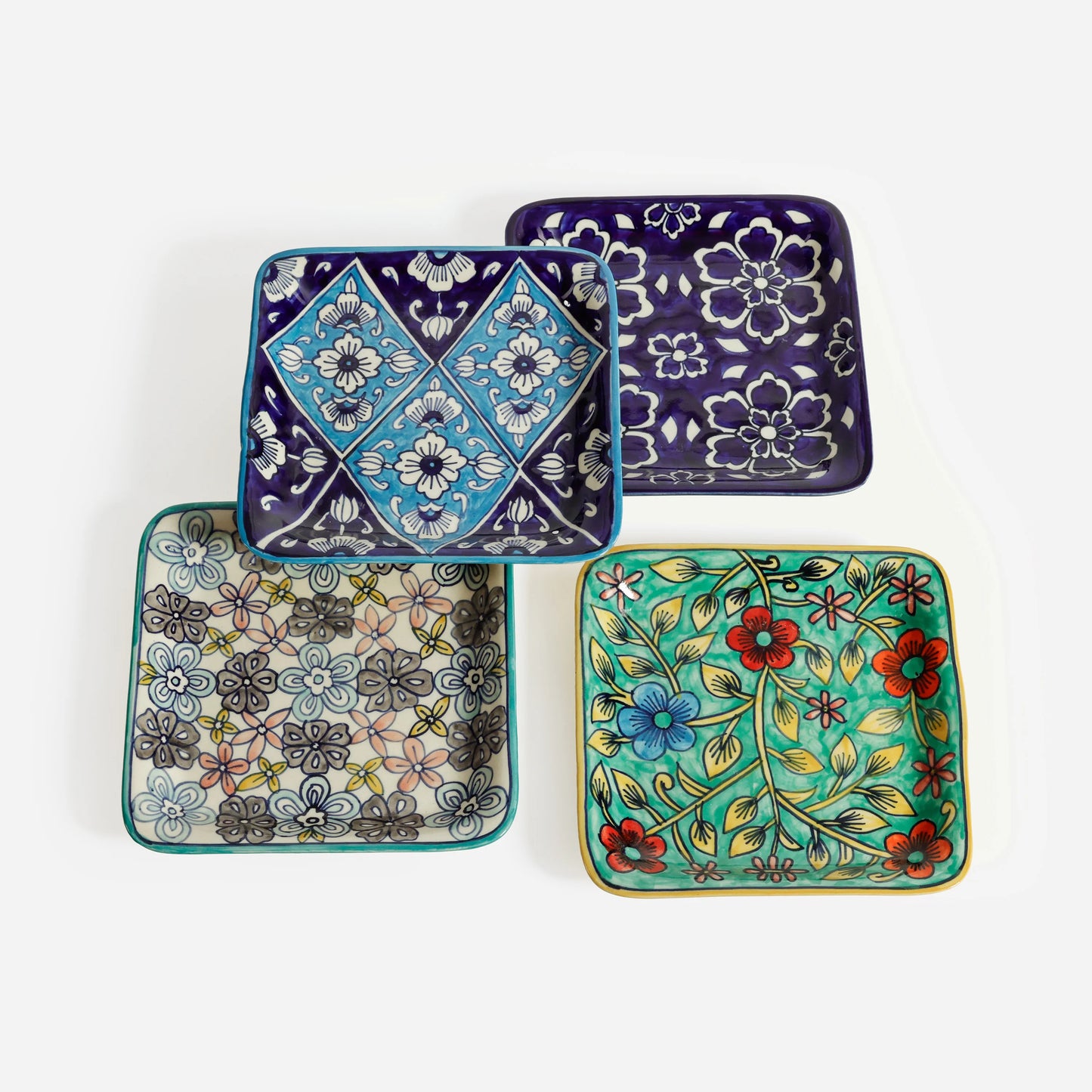 four assorted square ceramic plates with floral and geometric patterns on a white background