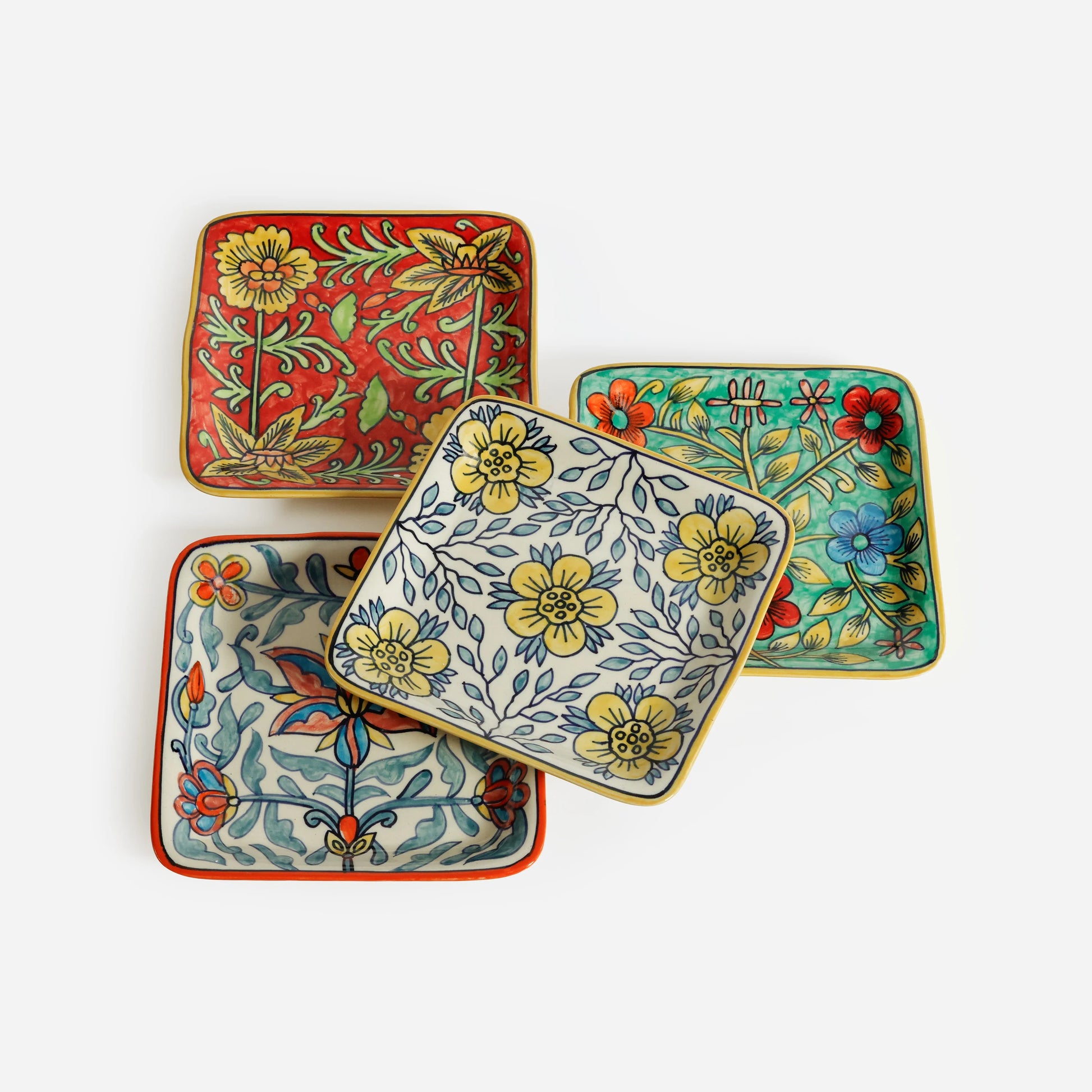 four assorted colorful square plates with floral patterns layered together on a white background