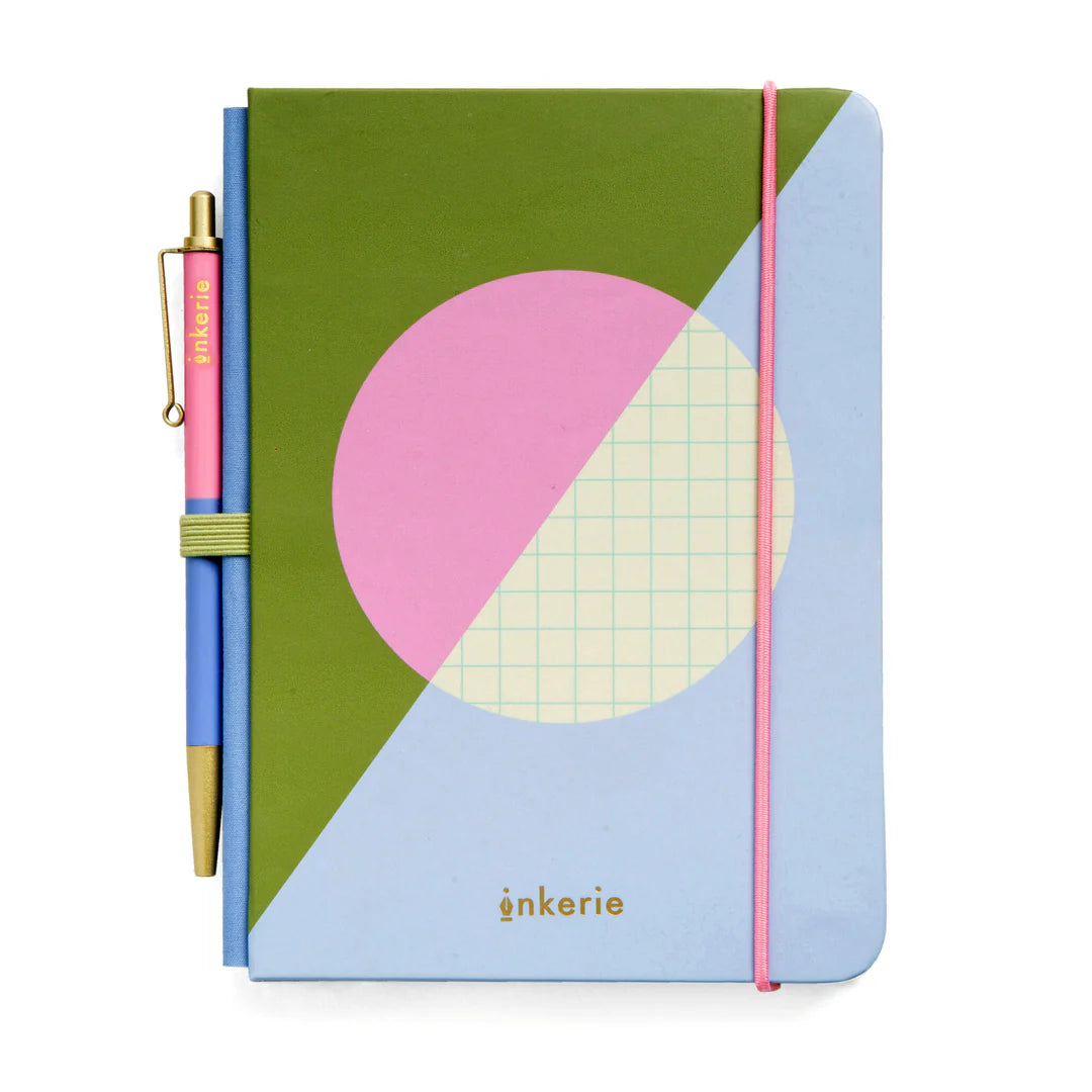 small notebook with green, blue, and pink cover and blue and pink pen in loop on its spine.