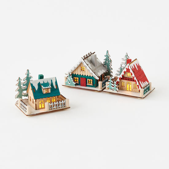 Scandinavian style lighted holiday lodges with a green, red, and white color scheme, featuring battery-operated lights and surrounded by mini trees.
