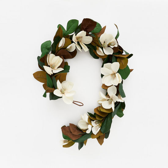A decorative garland featuring artificial magnolia leaves and flowers in shades of green, brown, and white.