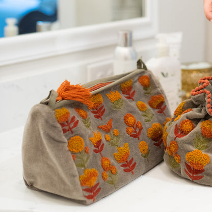 taupe zipper bag with floral embroidery on a bathroom counter.