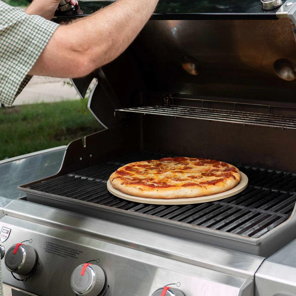 person opening grill showing round baking stone with a pizza on it inside