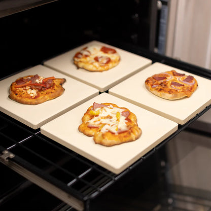4 small baking stones in an oven with a pizza on each one