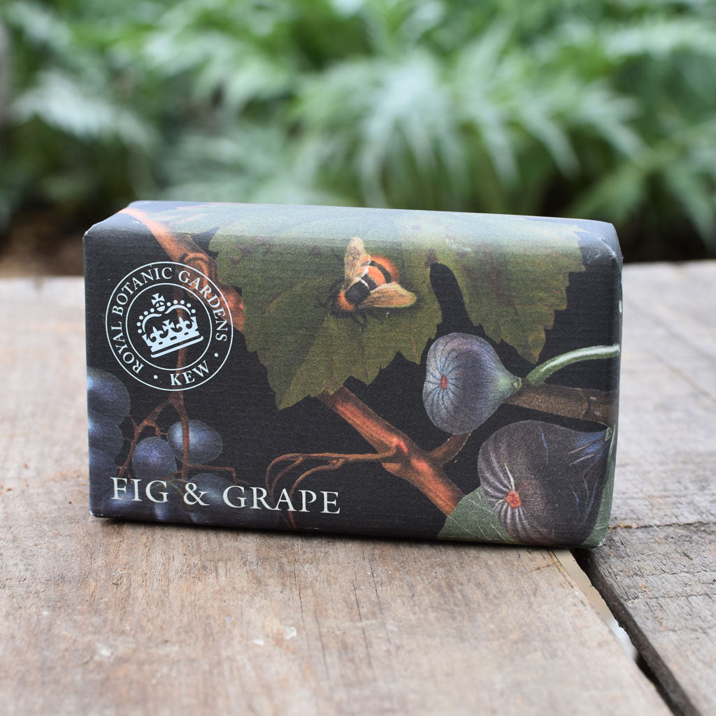 Bar of soap with 'Fig & Grape' design on a wooden surface with greenery in the background