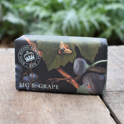 Bar of soap with 'Fig & Grape' design on a wooden surface with greenery in the background