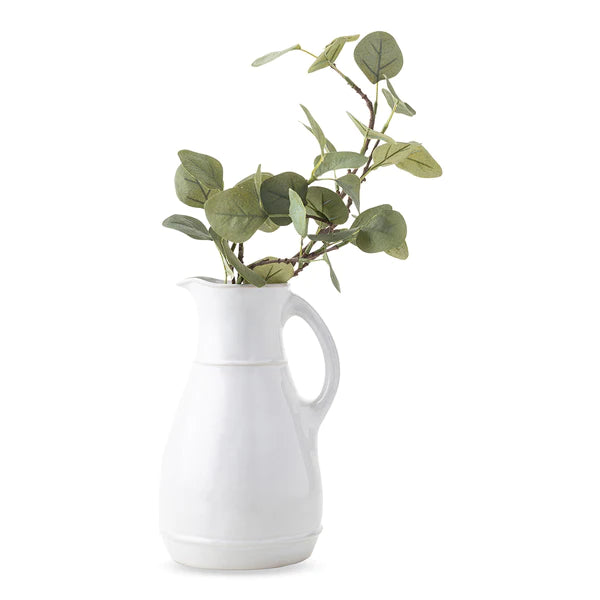 white ceramic pitcher with green plant stems coming out the the opening on a white background