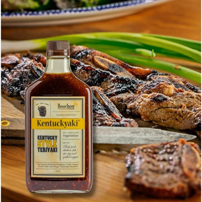 bottle of Kentuckyaki with grilled meats in the background.