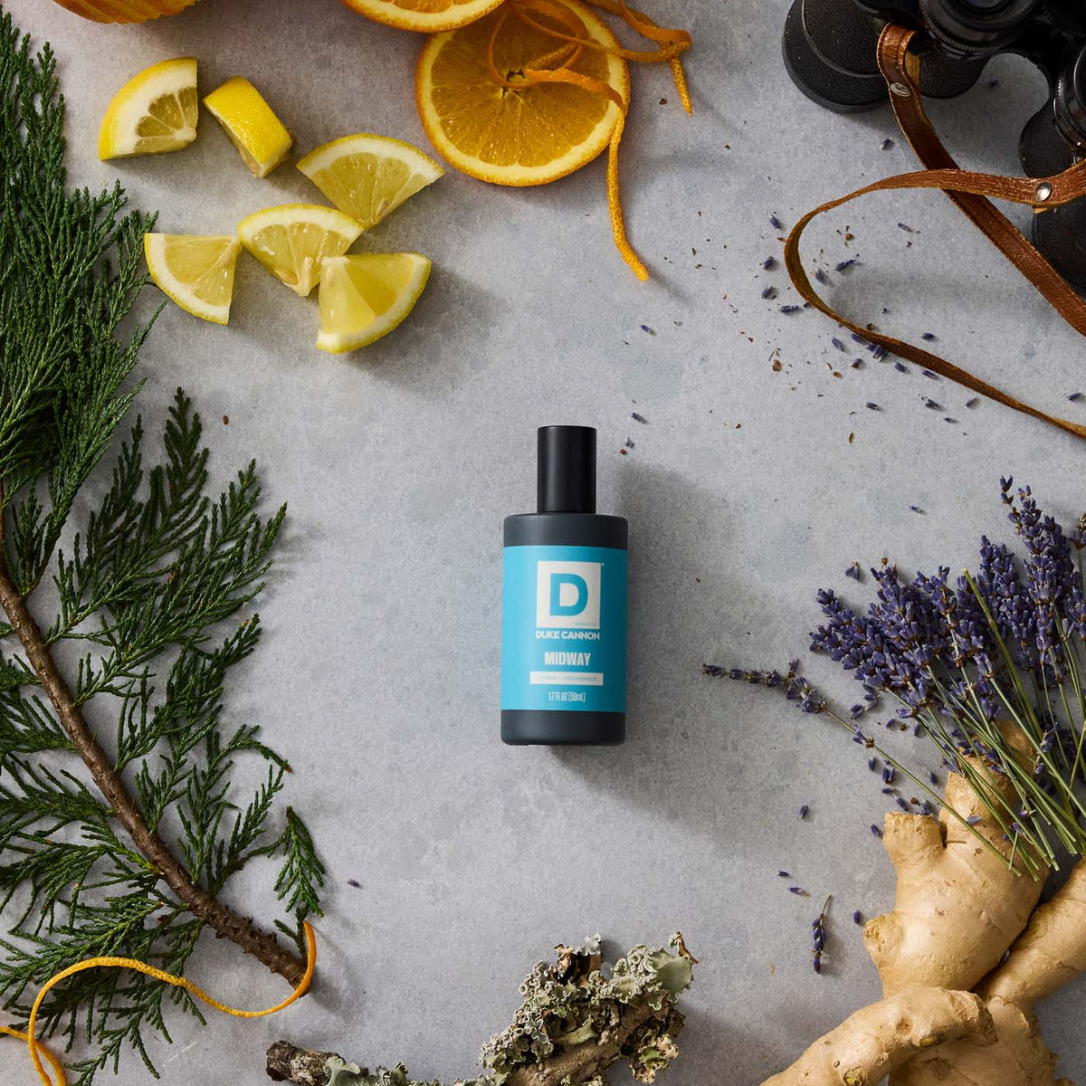 Midway Proper Cologne bottle on a stone background surrounded by citrus, cedar branch, and ginger