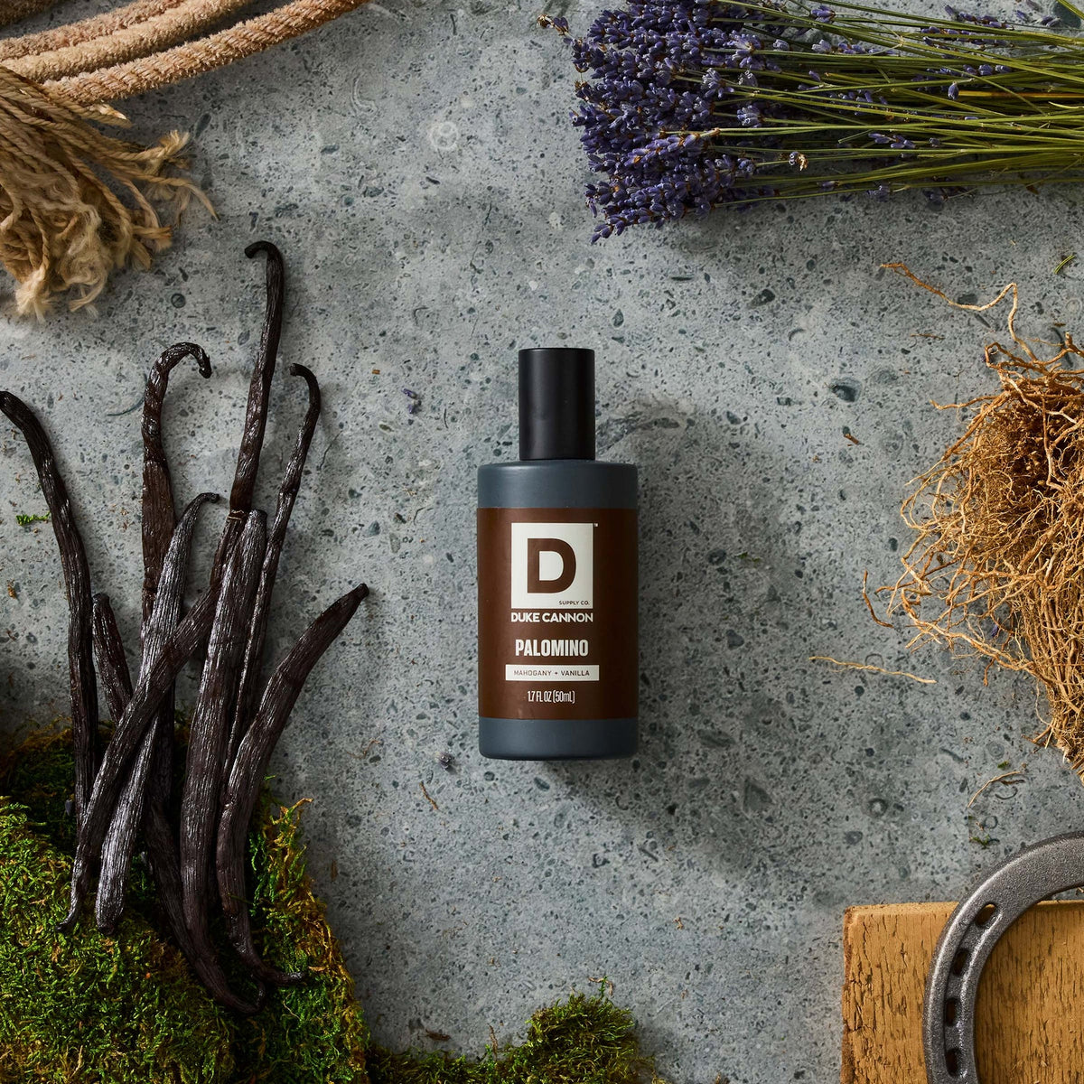 Palomino Proper Cologne bottle on stone background surrounded by vanilla bean, dried flower stems and a wood block