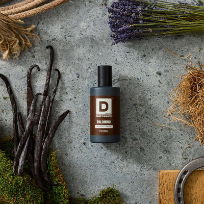 Palomino Proper Cologne bottle on stone background surrounded by vanilla bean, dried flower stems and a wood block