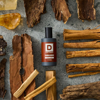 Sandalwood proper cologne bottle on a stone background next to strips of wood and chunks of amber