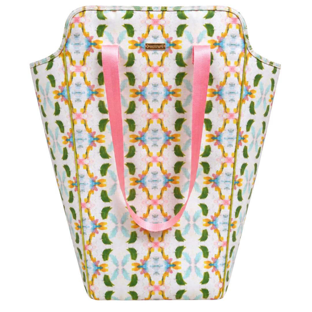 Laura Park Designs Dogwood Laundry Bag with a white background and a colorful geometric floral pattern in green, yellow, and blue, featuring two pink handles.