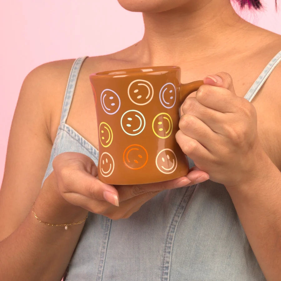 Person holding a brown mug with smiley face patterns against a pink background