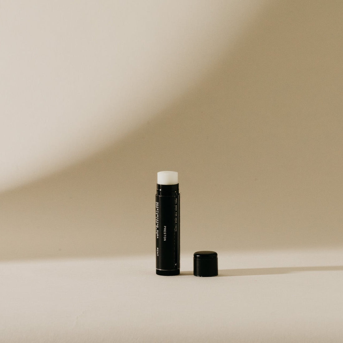 Black lip balm tube with cap set next to it on a beige background