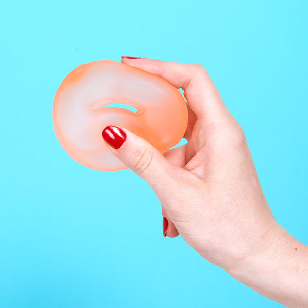 Hand holding a pale orange silicone stress ball loop against a blue background