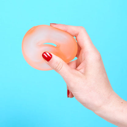 Hand holding a pale orange silicone stress ball loop against a blue background