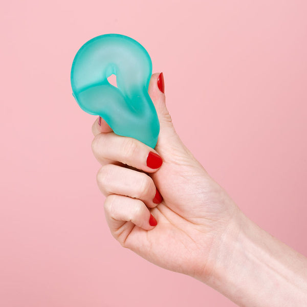 Hand holding a teal silicone stress ball loop against a pink background