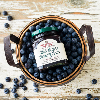 top view of a basket filled with blueberries and a jar of Wild Maine Blueberry Jam laying on it.