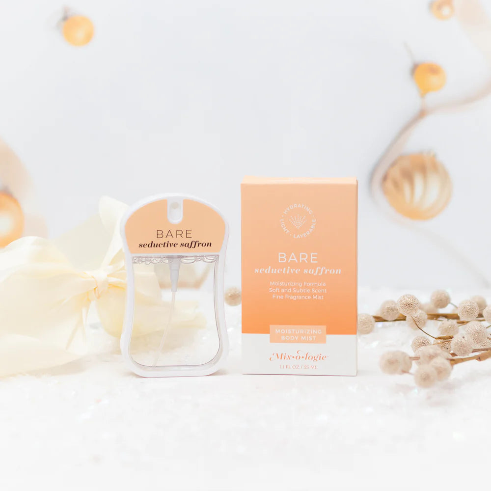 A bottle of Bare Reductive Saffron body mist and its matching box, styled with soft cream flowers and dried botanicals on a white surface.