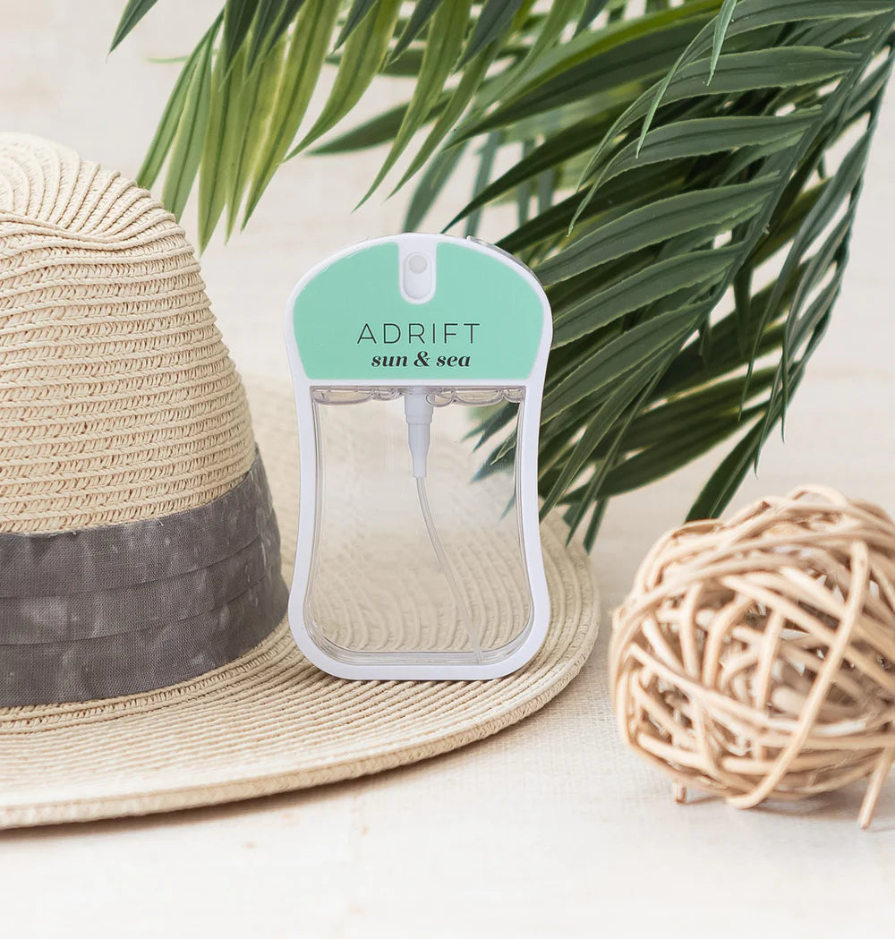 Adrift sun & sea' body mist on a straw hat and beach ball with palm leaves in the background.