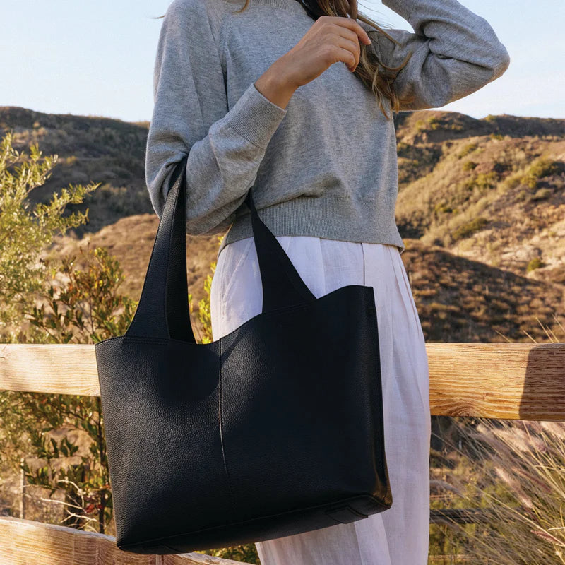 person standing among the countryside carrying a black via tote.