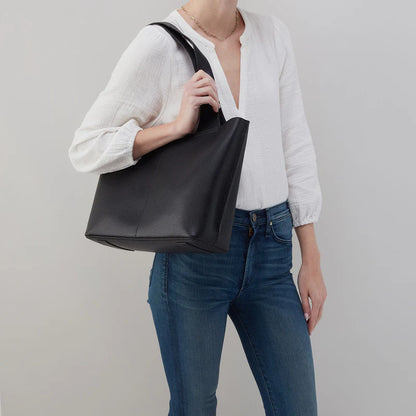 person wearing jeans and a white top carrying a black vida tote on their shoulder.