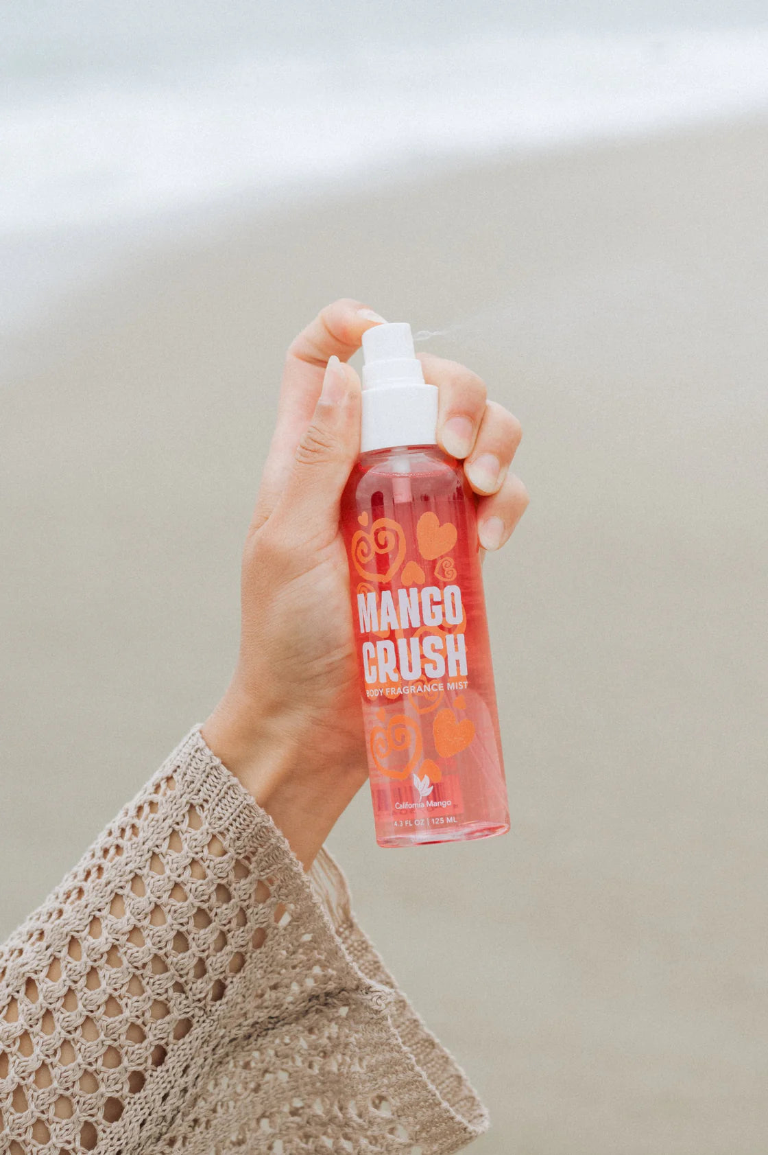 Hand holding a 'Mango Crush' spray bottle against a neutral background