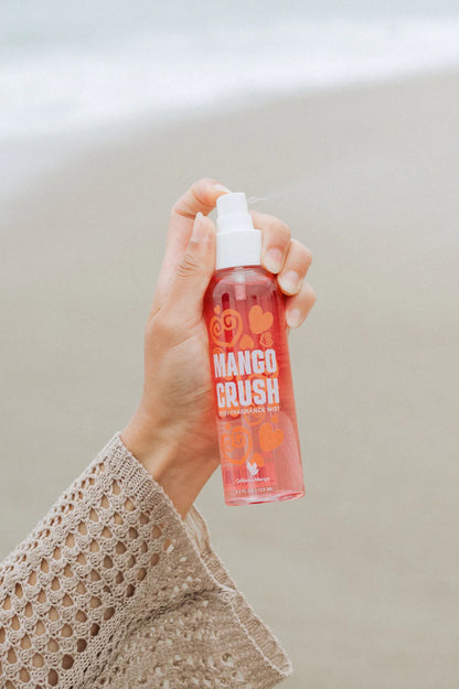 Hand holding a 'Mango Crush' spray bottle against a neutral background