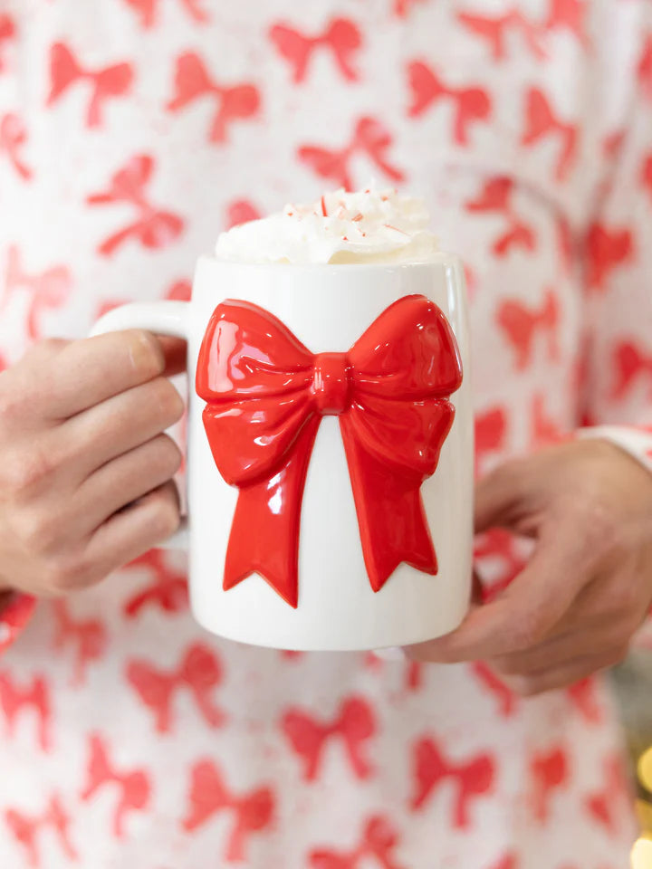 person holding white mug with red bow design. mug is topped with cream.