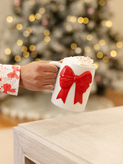 person holding bow mug with out stretched arm and lit tree in the background.