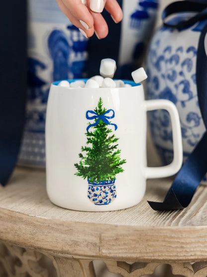 Festive and fancy mug set on a wooden table with hand dropping marshmallows into it.