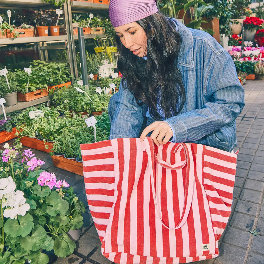 Woman with a red and pink striped bag in a garden center surrounded by plants and flowers